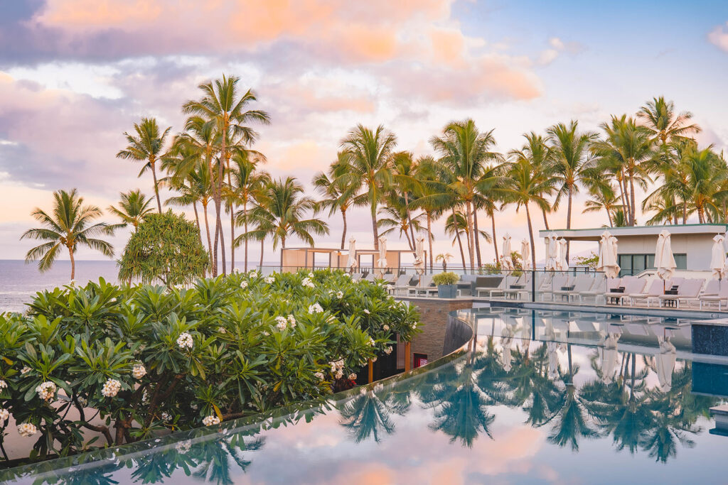 Tropical beachfront resort with infinity pool, palm trees, and ocean views at sunset.