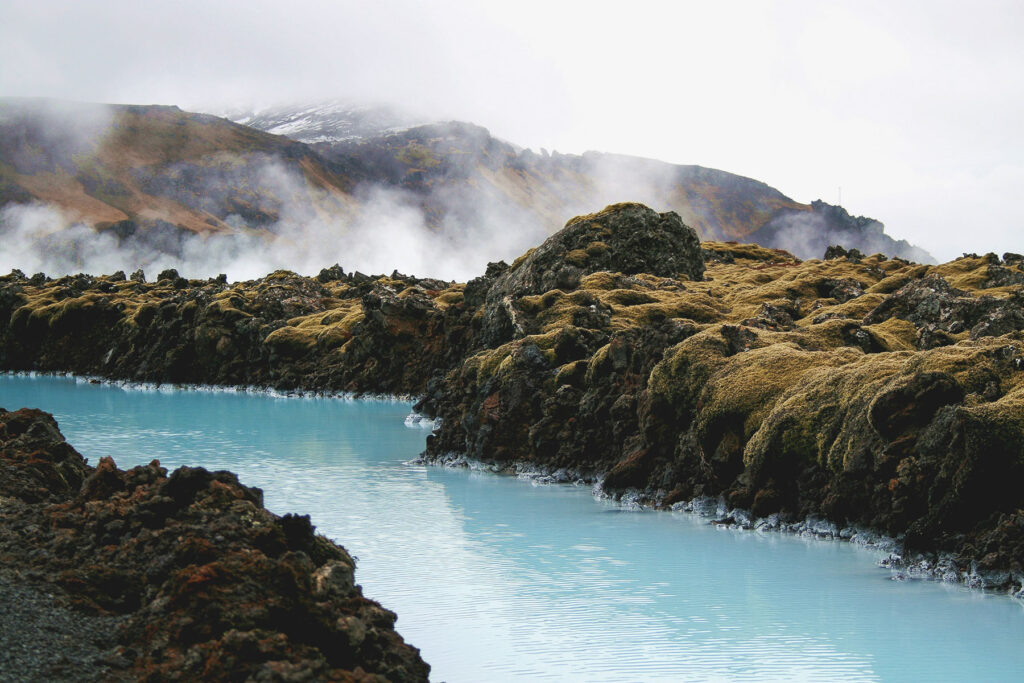 Geothermal Blue Lagoon in Iceland with milky blue water surrounded by dark volcanic rocks, moss, and rising steam.