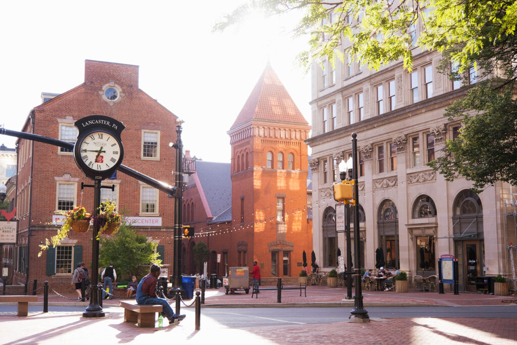 Historic downtown Lancaster, Pennsylvania with street clock, brick buildings, and people enjoying a sunny afternoon.