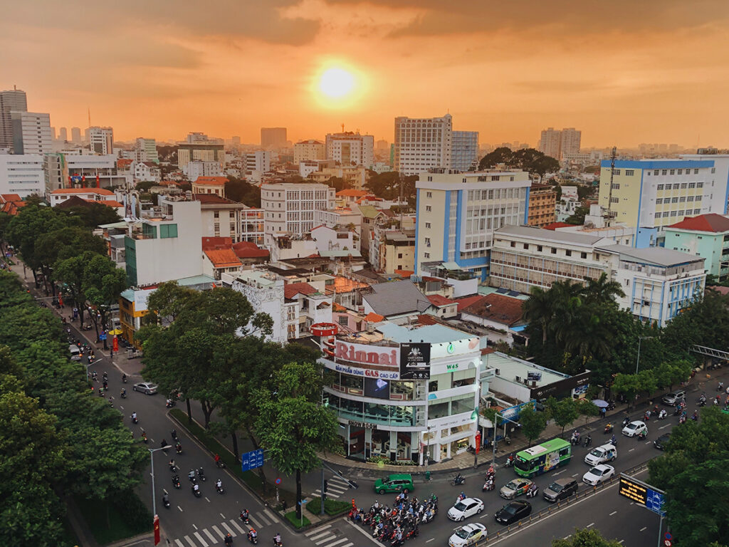 Sunset over Ho Chi Minh City skyline with busy streets, motorbikes, and buildings bathed in warm light.