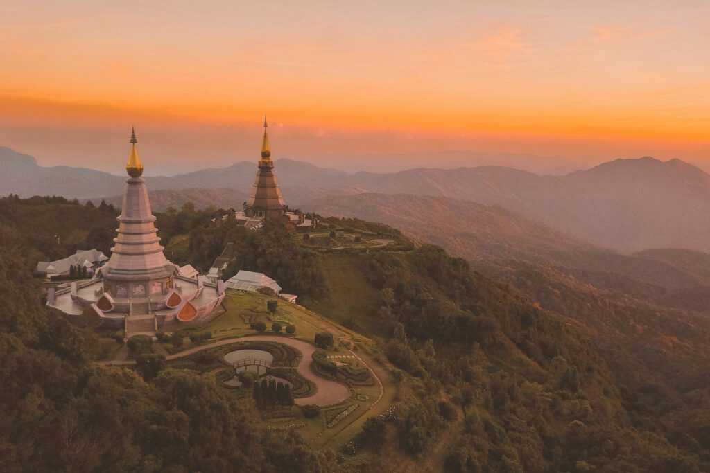Mountain temple pagodas at sunrise in Chiang Mai, Thailand with golden light over misty hills.