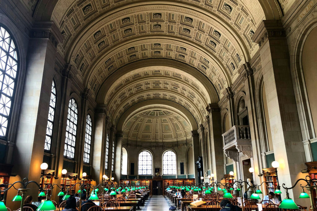 Grand historic library reading room with arched ceilings, green desk lamps, and long wooden tables.