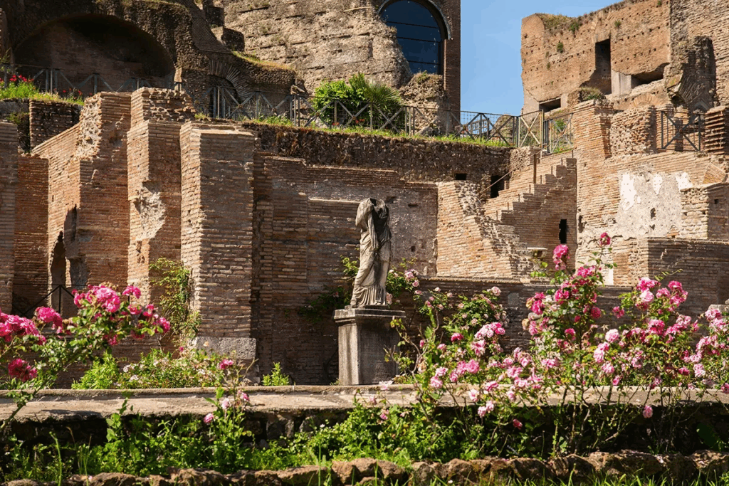 Ancient Roman Forum ruins with classical statue and blooming pink roses in foreground, beautiful example of things to do in Rome in spring at historic sites