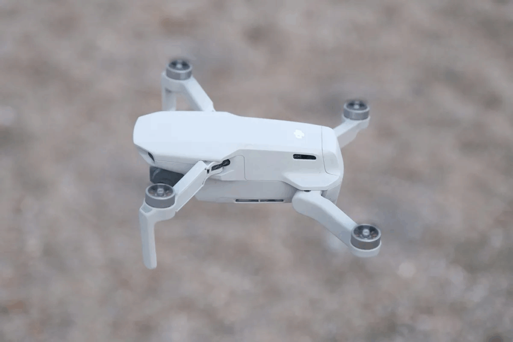 White DJI Mini 4 Pro drone hovering against gray background showing compact foldable design, top travel camera gear for aerial travel photography equipment