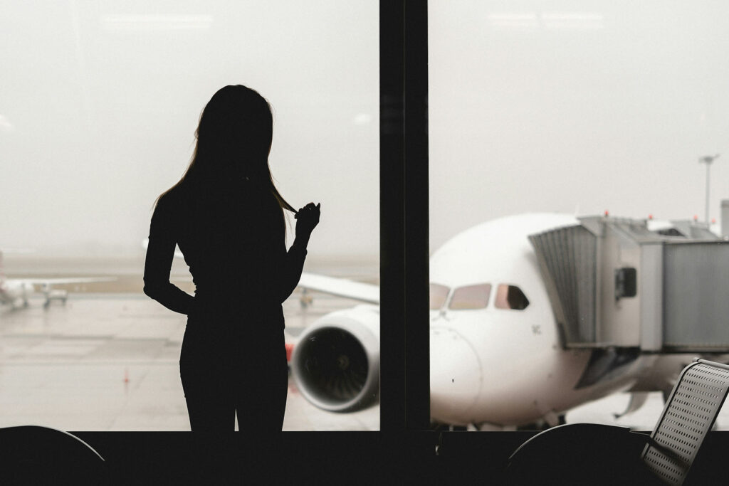 Silhouette of a woman standing by an airport window looking at an airplane at the gate.