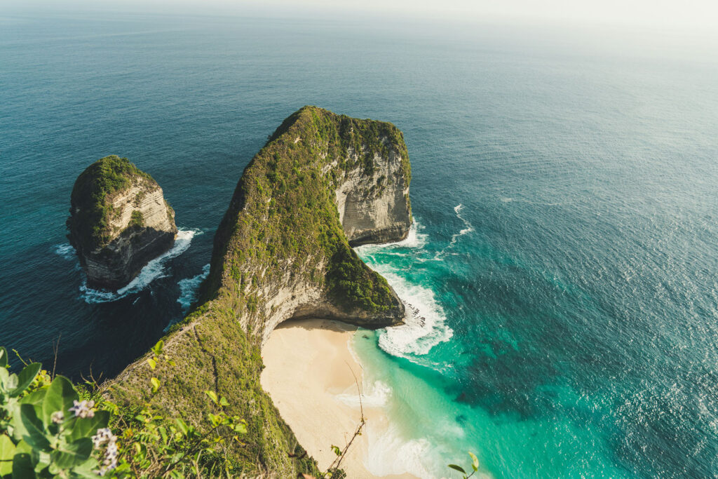 Aerial view of a dramatic cliffside beach with turquoise water and towering rock formations at Kelingking Beach in Nusa Penida, Bali.