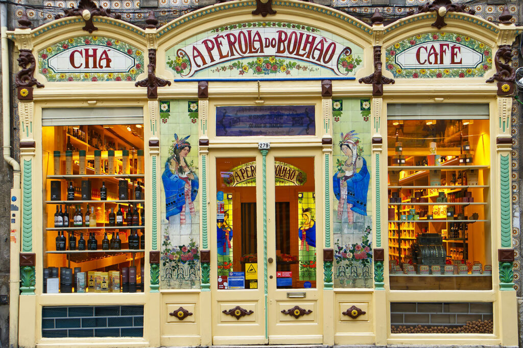 Historic storefront of A Pérola do Bolhão in Porto, Portugal, featuring ornate tiles, painted figures, and a traditional café and tea shop display.