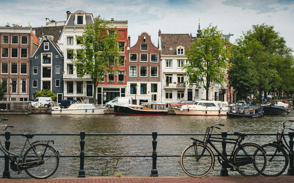Canal in Amsterdam lined with historic buildings, parked bicycles, and boats along the water.