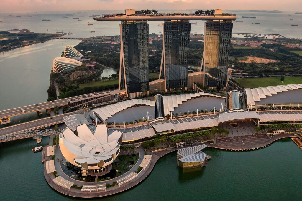 Aerial view of Marina Bay Sands in Singapore at sunset, with the iconic rooftop infinity pool, waterfront skyline, and surrounding gardens.