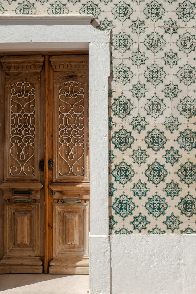 Traditional wooden door with decorative ironwork next to patterned ceramic tiles on a building facade in Portugal.