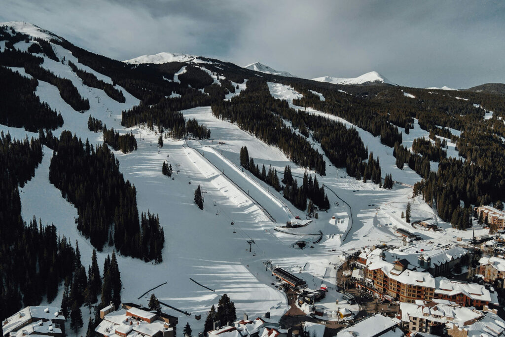Aerial view of a snowy ski resort in the mountains, with ski slopes, chairlifts, and alpine village buildings surrounded by forest