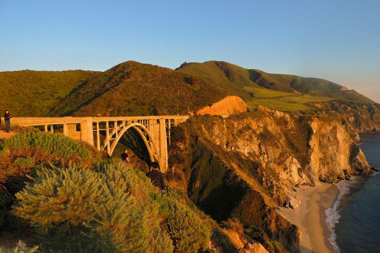 Bixby Creek Bridge in Big Sur at golden hour overlooking rugged cliffs and the Pacific Ocean coastline.