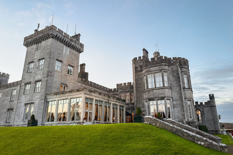 Exterior of a historic Irish castle hotel with stone towers and manicured green lawn at dusk.