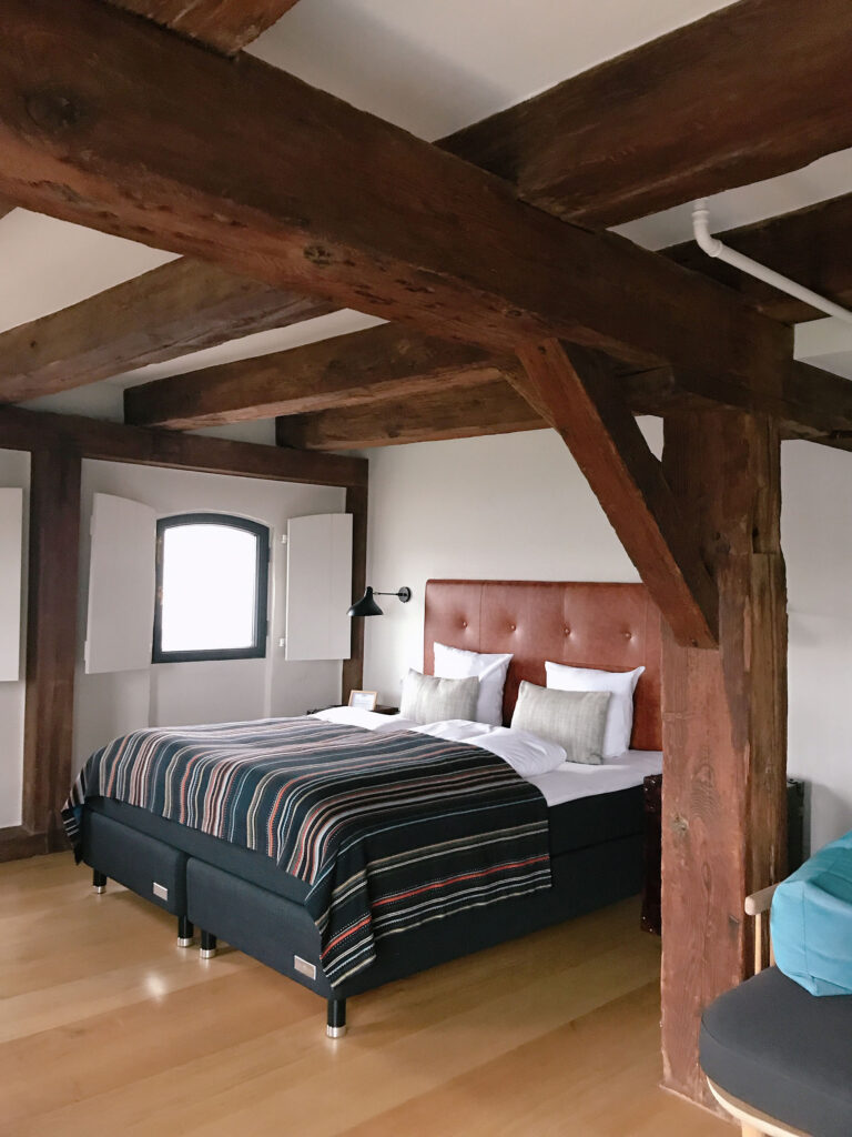 Cozy guest room at 71 Nyhavn Hotel in Copenhagen featuring exposed wooden beams, Scandinavian design details, warm natural tones, and a plush bed beside charming historic windows. Nastasia Yakoub. All rights reserved. No reposts, reuse, or distribution without written permission.