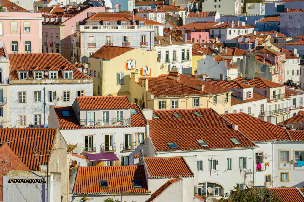 Colorful Lisbon rooftops and pastel buildings in the historic Alfama neighborhood, featuring traditional terracotta tiles and layered city architecture under warm sunlight.